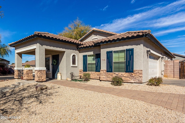 mediterranean / spanish-style house with a garage, stone siding, a tile roof, and stucco siding