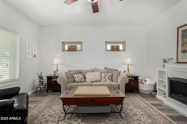 living room featuring a glass covered fireplace, wood finished floors, a ceiling fan, and baseboards