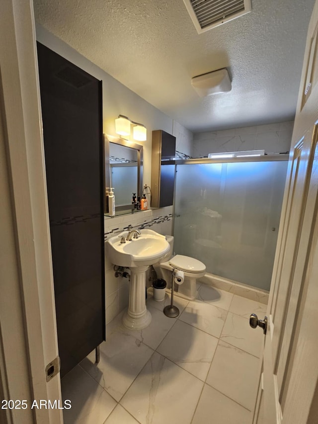 bathroom featuring a shower with shower door, toilet, and a textured ceiling