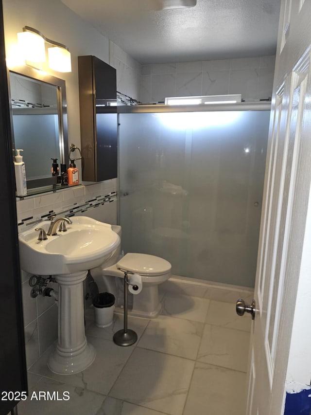 bathroom with decorative backsplash, toilet, a shower with door, and a textured ceiling