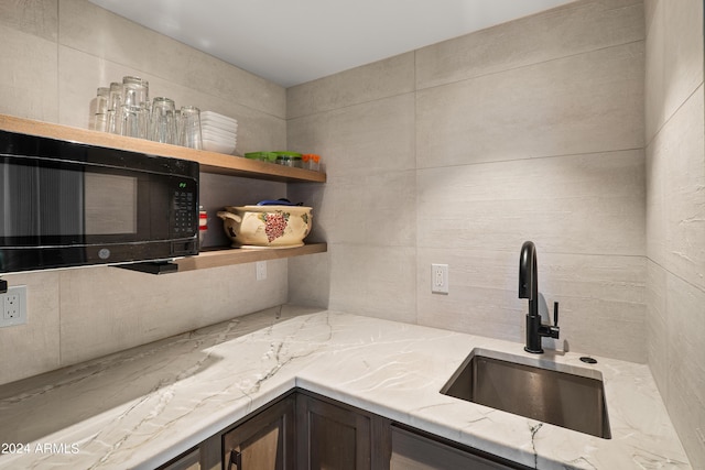 kitchen with light stone countertops, open shelves, a sink, decorative backsplash, and black microwave