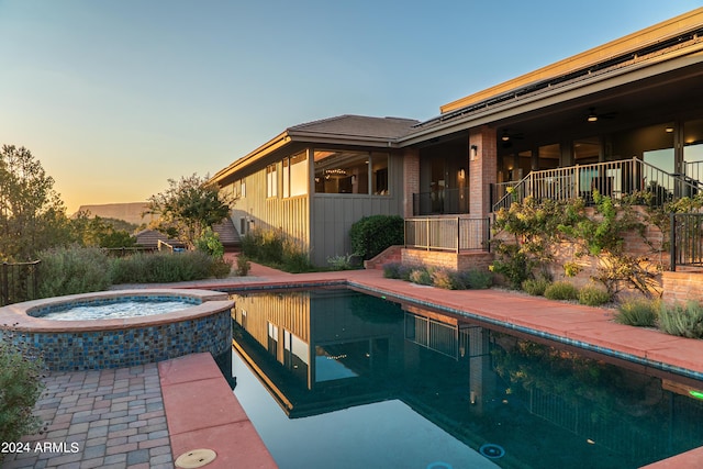 pool at dusk with a pool with connected hot tub