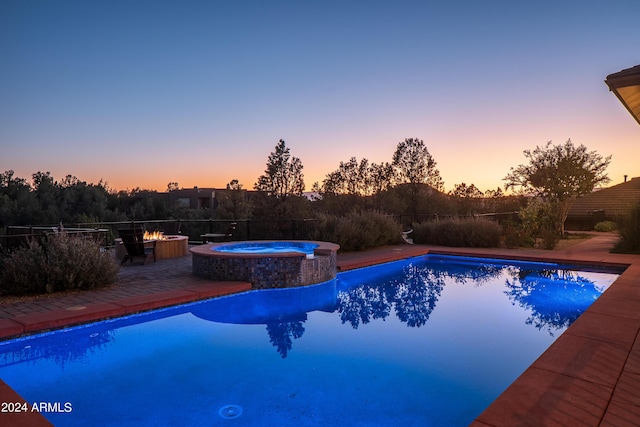 pool at dusk with a patio area and a pool with connected hot tub