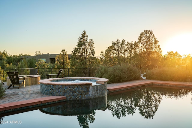 pool at dusk featuring a pool with connected hot tub