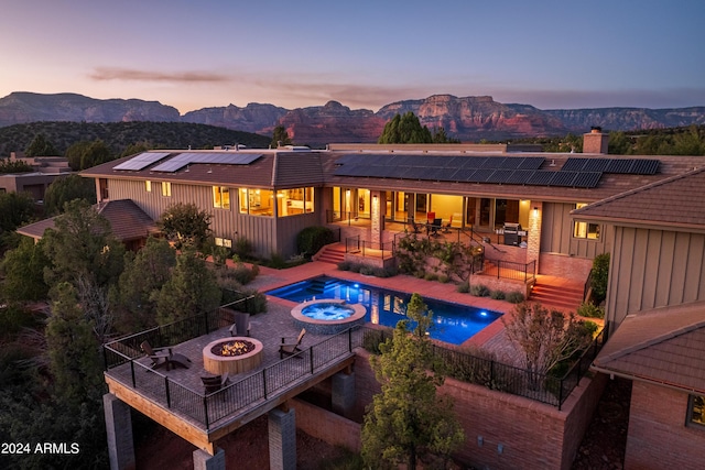 back of property at dusk with a mountain view, a fire pit, and a patio area