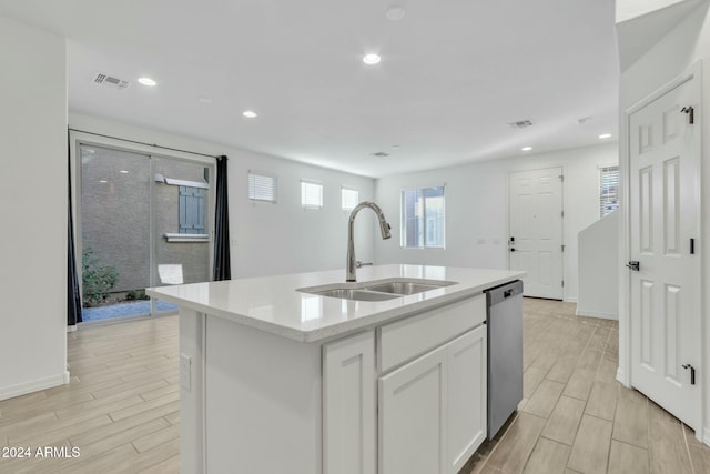 kitchen with light stone countertops, dishwasher, sink, a kitchen island with sink, and white cabinets