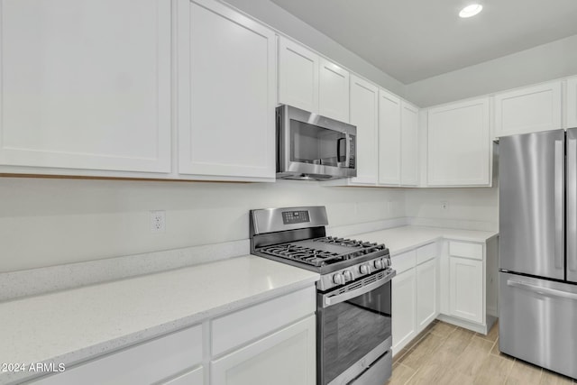 kitchen with light stone counters, light hardwood / wood-style flooring, white cabinets, and appliances with stainless steel finishes