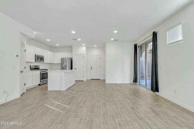 kitchen with a center island with sink, white cabinets, sink, light wood-type flooring, and stainless steel appliances