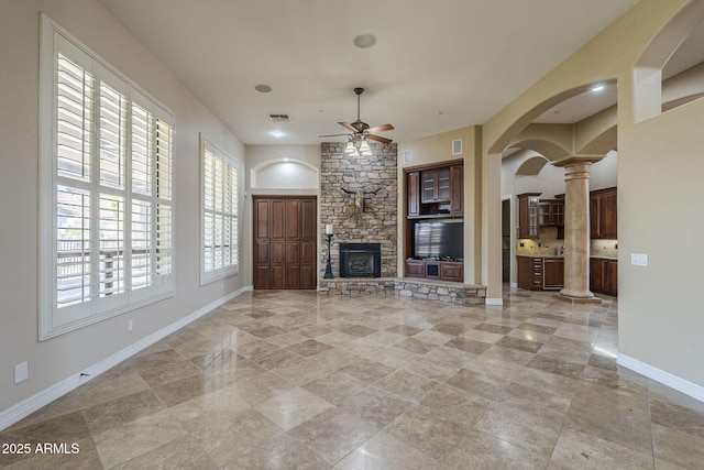 10033 W Jj Ranch Rd, Peoria, AZ 85383 - unfurnished living room featuring decorative columns, a ceiling fan, baseboards, arched walkways, and a stone fireplace