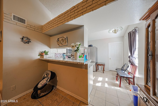 9021 W Mulberry Dr, Phoenix, AZ 85037 - kitchen with a textured ceiling, a peninsula, light tile patterned flooring, and visible vents