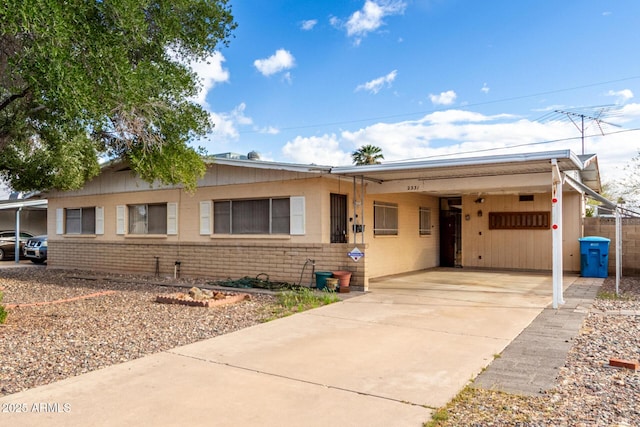 ranch-style house with an attached carport, concrete driveway, brick siding, and fence