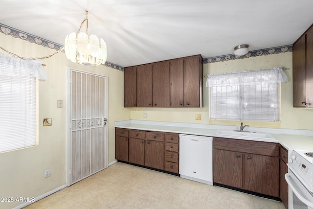 kitchen featuring white appliances, a sink, light countertops, pendant lighting, and a chandelier