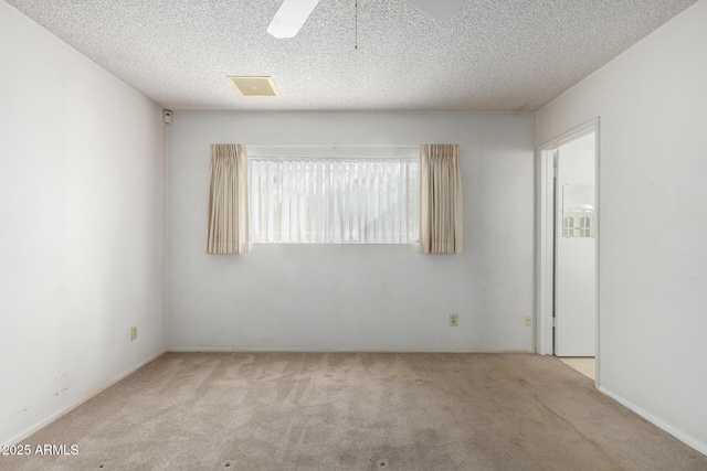 carpeted spare room featuring a textured ceiling, visible vents, and ceiling fan