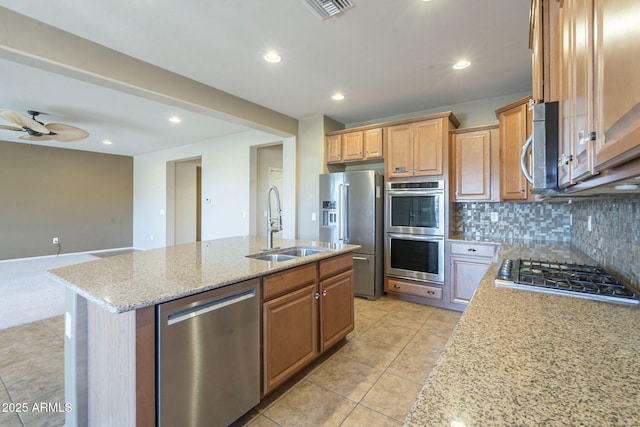 kitchen featuring sink, appliances with stainless steel finishes, tasteful backsplash, light stone countertops, and a center island with sink