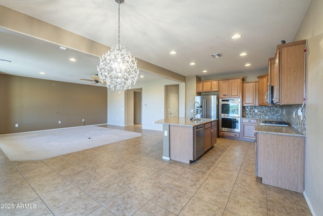 kitchen featuring decorative light fixtures, tasteful backsplash, sink, stainless steel appliances, and a center island with sink