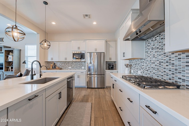 kitchen with light wood-type flooring, backsplash, wall chimney exhaust hood, stainless steel appliances, and white cabinets