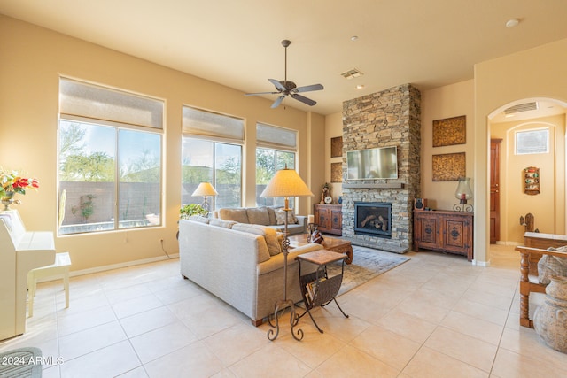 living room with ceiling fan, a stone fireplace, and light tile patterned floors