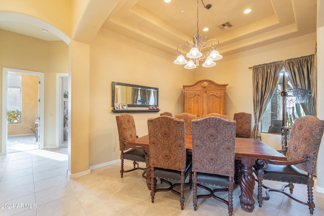 tiled dining area with a wealth of natural light, a high ceiling, an inviting chandelier, and a raised ceiling