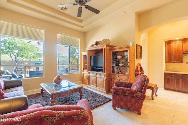 tiled living room with a raised ceiling and ceiling fan