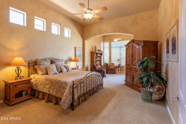 bedroom with ceiling fan, light carpet, and a high ceiling