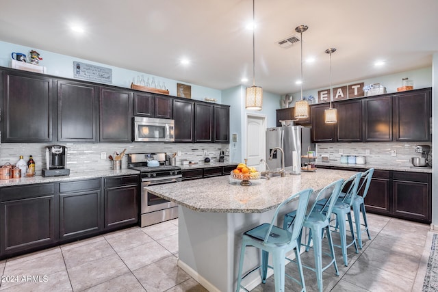 kitchen with a kitchen island with sink, stainless steel appliances, dark brown cabinetry, and a breakfast bar