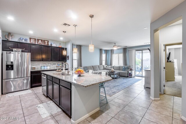 kitchen featuring hanging light fixtures, appliances with stainless steel finishes, light stone counters, sink, and a kitchen island with sink