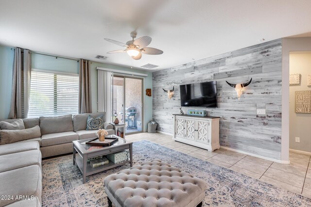 living room featuring ceiling fan, wood walls, and light tile patterned flooring