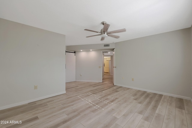 spare room featuring a barn door, light hardwood / wood-style flooring, and ceiling fan