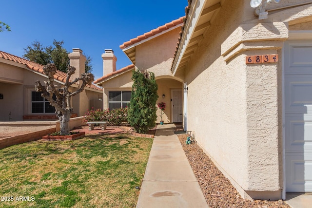 doorway to property featuring a tiled roof, a yard, a garage, and stucco siding