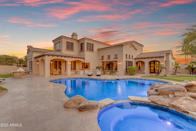 back of property featuring a tile roof, a patio area, a pool with connected hot tub, and stucco siding