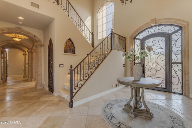 entrance foyer with visible vents, arched walkways, a towering ceiling, and baseboards