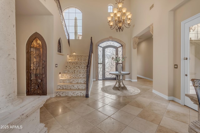 tiled foyer featuring stairway, arched walkways, an inviting chandelier, baseboards, and a towering ceiling