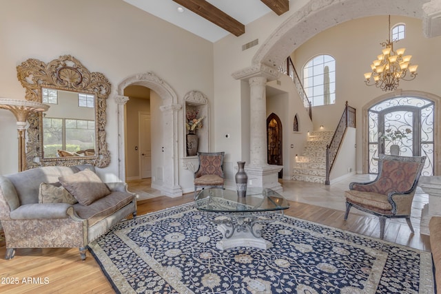 living area with visible vents, wood finished floors, arched walkways, decorative columns, and a chandelier