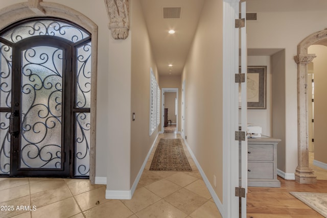 foyer with arched walkways, visible vents, baseboards, and decorative columns