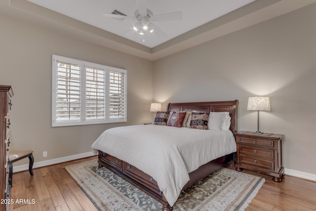 bedroom with visible vents, a tray ceiling, baseboards, and wood finished floors