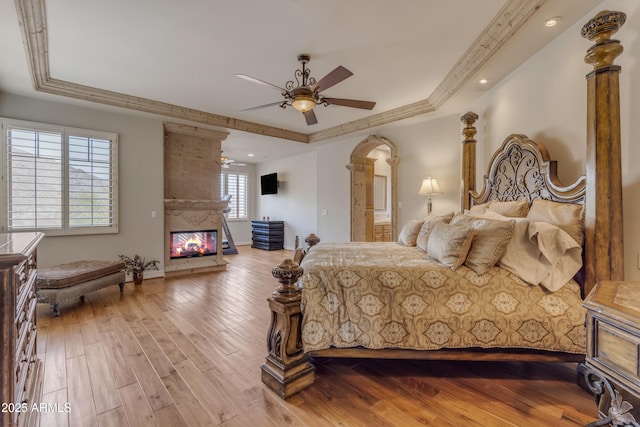 bedroom featuring a fireplace, crown molding, a tray ceiling, and wood finished floors