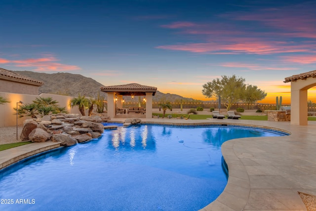 pool at dusk with a gazebo, a mountain view, an in ground hot tub, and fence