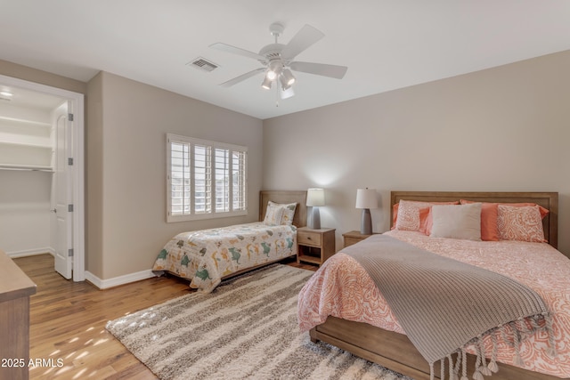 bedroom with visible vents, a walk in closet, baseboards, wood finished floors, and a ceiling fan