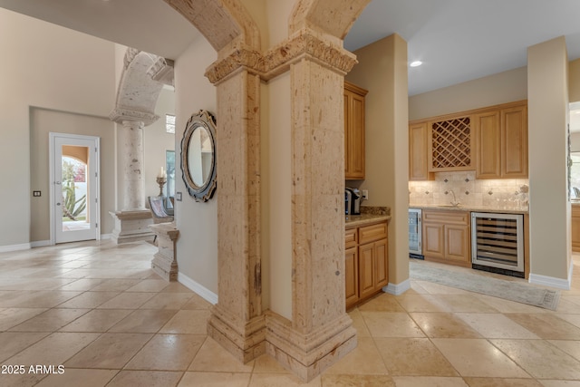 interior space featuring backsplash, beverage cooler, ornate columns, and a sink