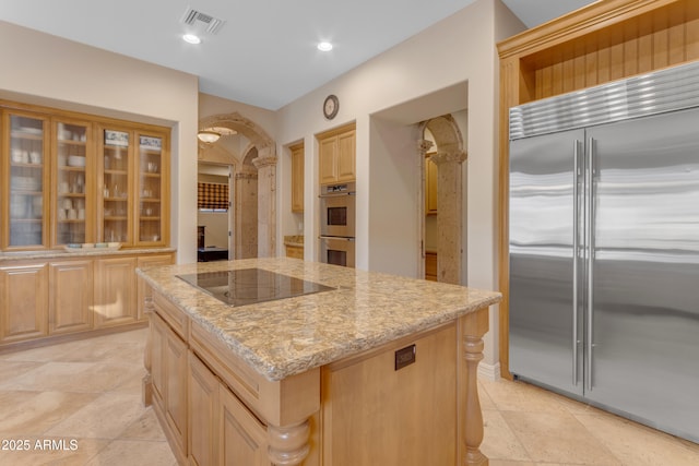 kitchen with light brown cabinets, light stone counters, a center island, stainless steel appliances, and arched walkways