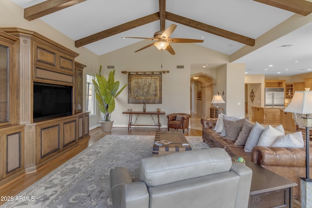 living room with light wood-type flooring, lofted ceiling with beams, arched walkways, baseboards, and ceiling fan