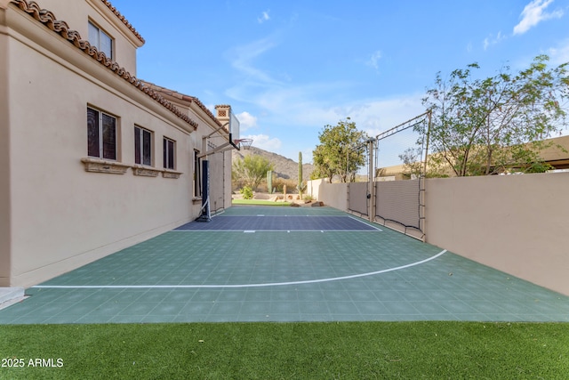 view of basketball court with basketball court, a mountain view, fence, and a gate