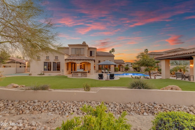 back of property at dusk featuring a fenced in pool, a tiled roof, a lawn, a fenced backyard, and a patio area