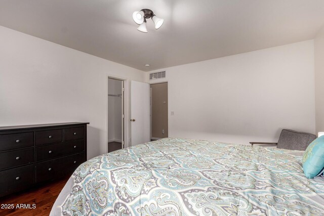 bedroom featuring a walk in closet, dark wood-style floors, and visible vents