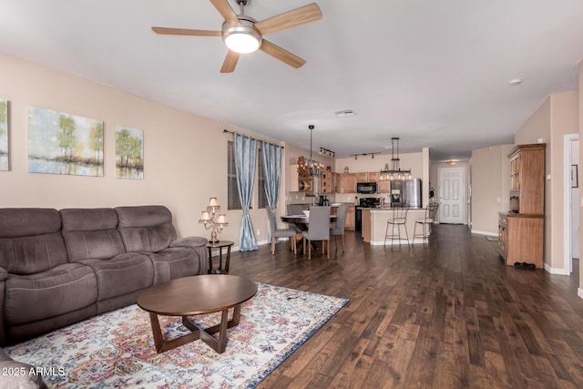 living area with baseboards, ceiling fan with notable chandelier, and dark wood-style floors