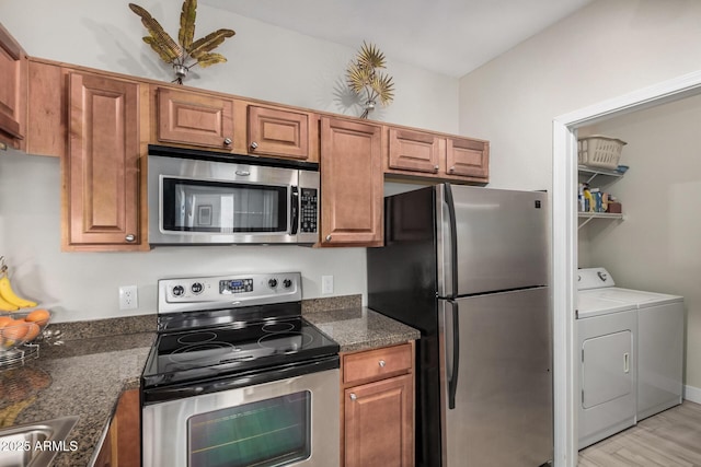 kitchen with sink, light hardwood / wood-style flooring, dark stone countertops, stainless steel appliances, and washer and dryer