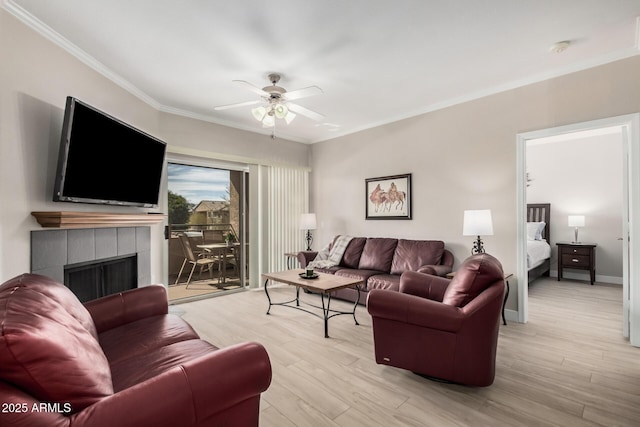 living room with ceiling fan, ornamental molding, a tiled fireplace, and light hardwood / wood-style flooring