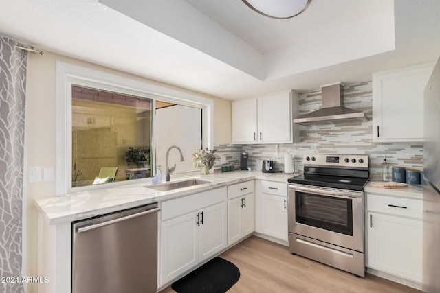 kitchen featuring sink, stainless steel appliances, white cabinetry, and wall chimney range hood