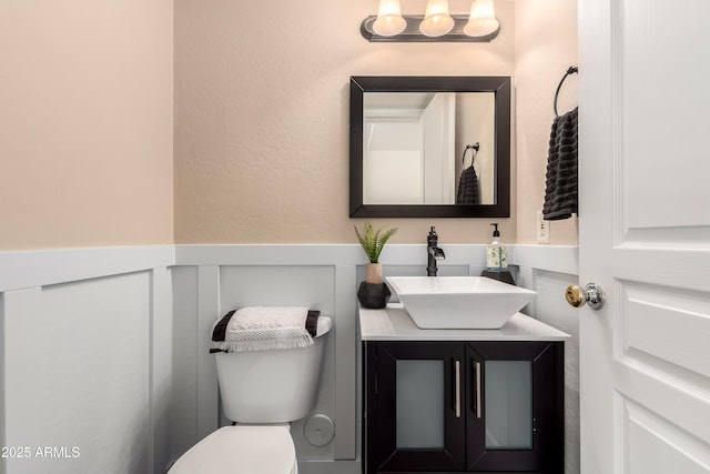 half bath with vanity, a wainscoted wall, and toilet