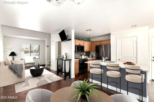 kitchen with light countertops, a kitchen island with sink, decorative backsplash, visible vents, and black appliances